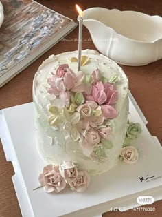 a white cake with flowers and a single candle on it sitting on top of a table