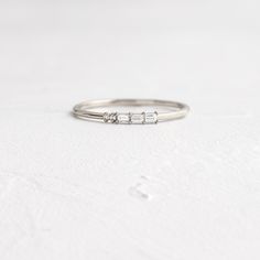 a white gold ring with three baguettes set in the middle, sitting on a plain surface