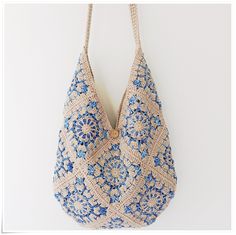 a crocheted bag hanging from a hook on a white wall with blue flowers