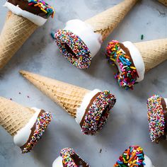 six ice cream cones with sprinkles and chocolate frosting in them on a table