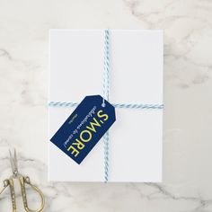 a gift wrapped in white paper with a blue tag on it next to some scissors