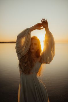 a woman in a white dress is standing by the water with her hands on her head