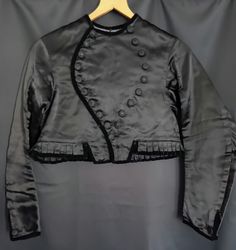 Satin Black Vintage Folklore Jacket. ▪︎●▪︎ The jacket originates from Germany and is part of a stunning traditional folklore costume. The outer fabric is in a rich black satin with velvet on the rim. Also decorated with stunning handcrafted buttons. The fit is in the style of a short bolero. A great look with high waisted jeans or skirts.   From ca. 1940s. ☆ ☆ ☆ handrafted traditional one of a kind ☆ A size S minus (small UK 8/European 36). Bust 45 cm/17.71" Shoulders 36 cm/14.17'' Length approx. 38 cm/14.96'' Necklace 16 cm/6.29" Arms 57 cm/22.44" -armhole 19 cm/7.48" -arm width15cm/5.90" -cuff 11 cm/4.33" ♡Super Rare Collectable♡ Fitted Black Silk Outerwear, Black Gothic Velvet Outerwear, Black Velvet Gothic Outerwear, Black Long Sleeve Ceremonial Outerwear, Traditional Black Ceremonial Outerwear, Traditional Fitted Evening Outerwear, Traditional Evening Outerwear For Winter, Black Satin Outerwear For Party, Black Satin Party Outerwear