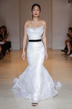 a woman in a white wedding dress walking down the runway with her hand on her hip