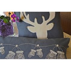 two gray pillows with silver sequins on them and a purple vase filled with flowers