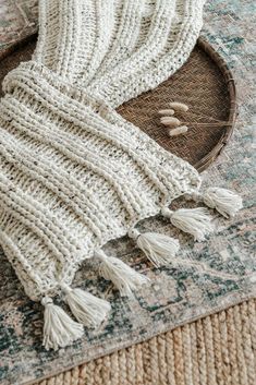 a white knitted scarf laying on top of a rug next to a wooden tray