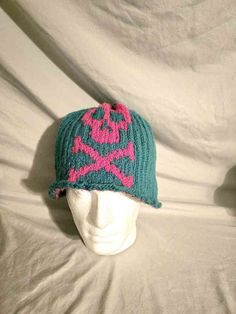 a white mannequin head wearing a green and pink knitted hat with skulls on it