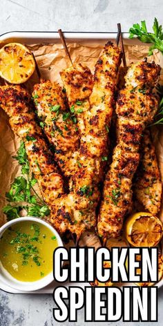 grilled chicken skewers with lemons and parsley on a tray next to dipping sauce