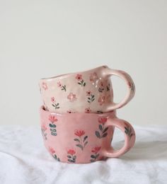 two pink mugs sitting on top of a white tablecloth covered bed next to each other