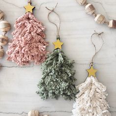 three christmas tree ornaments on a marble surface with wooden beads and star decorations around them