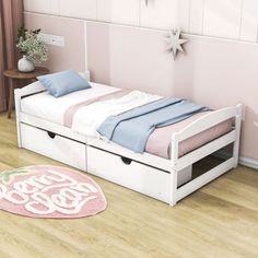 a bedroom with pink walls and wooden flooring has a white bed frame with drawers underneath it