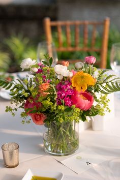 a vase filled with lots of colorful flowers on top of a white table covered in greenery