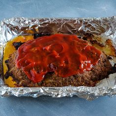 a meatloaf covered in ketchup and mustard on top of aluminum foil