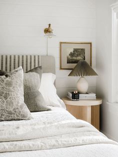 a bed with white sheets and pillows next to a lamp on a nightstand in a bedroom