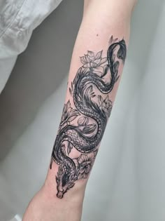 a woman's arm with a dragon and flowers tattoo on the left side of her arm