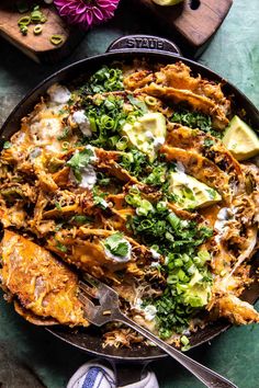 a skillet filled with chicken and vegetables on top of a wooden cutting board next to sliced avocado