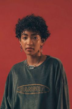 a woman with curly hair wearing a green sweatshirt and silver earring set, standing in front of a red background