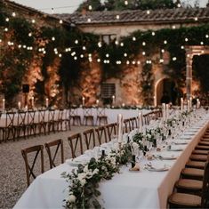 a long table is set up with white linens and greenery for an outdoor dinner