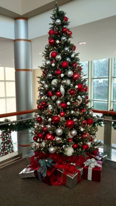 a christmas tree with red and silver ornaments in an office building, decorated for the holidays