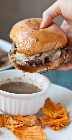 a person is dipping some kind of sauce into a hamburger on a plate with chips