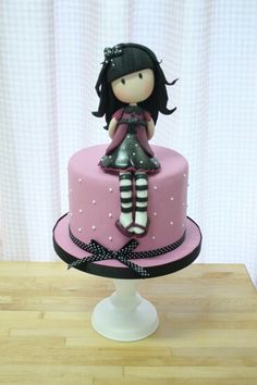 a pink and black cake with a doll on top, sitting on a wooden table