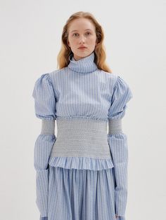 Editor's notesPuffed sleeves define our cotton-stretch victorian style top. Balance its proportions with flared jeans and sky-high wedges for a classic, chic look.- Victorian mood blouse- Combination color of sky blue stripe- High turtleneck with stitched edges- Long puff sleeves with smocked in the middle- Frilled hem - Button back closure- Smocked wide-waist band- Set up with smocked pants and skirt by EENKMeasurements(in.)- Size: XS, S, M- Shoulder: 15in / 15.51in / 15.98in- Chest: 35.63 Fitted Smocked Top For Daywear In Fall, Fitted Smocked Top For Fall Daywear, Fitted Cotton Smocked Daywear Top, Fitted Cotton Smocked Top For Daywear, Elegant Fitted Smocked Top With Elastic Sleeves, Blue Puff Sleeve Smocked Top With Smocked Cuffs, Spring Fitted Smocked Top With Blouson Sleeves, Light Blue Fitted Smocked Top For Spring, Fitted Light Blue Smocked Top For Spring