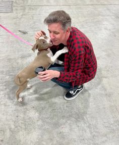 a man kneeling down next to a dog holding a can in it's mouth