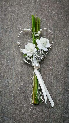 a bouquet of flowers on the ground with white ribbons and pearls hanging from it's center