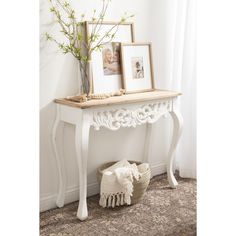 a white console table with two pictures on it and a basket full of flowers next to it