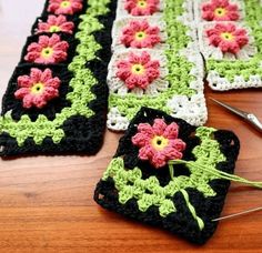 two crocheted squares with pink and green flowers sitting on top of a wooden table