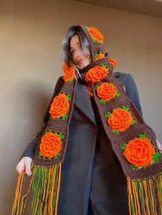 a woman wearing an orange and brown crocheted scarf with flowers on it's edge