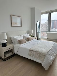 a large white bed sitting in a bedroom next to a tall window with city view