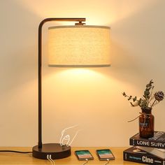 a table lamp sitting on top of a wooden desk next to a book and phone