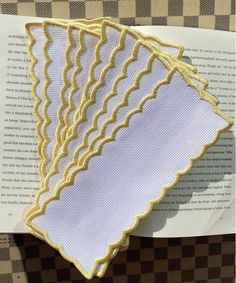 three pieces of cloth on top of an open book with gold thread and scalloped edges