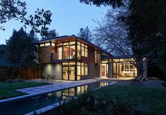 a modern house is lit up at night in the evening with its large windows open