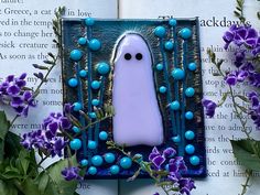 a book with purple flowers and blue beads on it, next to a white ghost