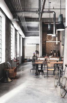 an industrial style kitchen and dining area with exposed pipes, windows, and tables in the center