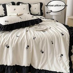 a white bed with black ruffles and pillows on it's coverlet