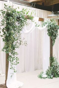 an indoor ceremony with greenery and white drapes