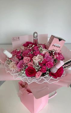 a bouquet of pink roses in a pink gift box with some lipstick and perfume bottles