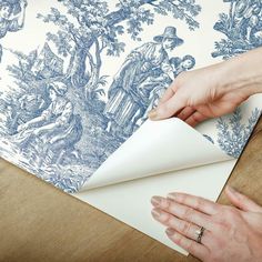 a person is making a wallpaper with blue toiler designs on it and another hand reaching for the paper