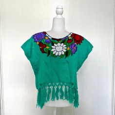 Very beautiful handmade Mexican Huipil Embroidered blouse. Great for the summer, they are very light and comfortable. Made In Mexico By: Mexican Artisans For: Women Size: M/L (view size chart) Color: teal | multi Details: - Material: Cotton - Non-stretch - Embroidery thread - Pullover closure - Boat neckline - Tassels on end Washing Instructions: One thing to remember when you wash a shirt, is to wash them with similar colors, and to use cold or warm water. A gentle detergent is always recommended as well. If you are concerned about damaging your shirt, send it to a dry cleaner to clean. Drying Instructions: If you need to dry your shirts with a dryer, always option for low heat or no heat. To prevent your shirt from shrinking, the recommended way to dry your shirt is to air dry it. If pos Summer Beach Blouse With Crew Neck, Summer Crew Neck Blouse For Beach, Summer Crew Neck Blouse For The Beach, Embroidered Short Sleeve Beach Shirt, Embroidered Short Sleeve Shirt For Beach, Summer Cotton Embroidered Crew Neck Top, Embroidered Summer Shirt For The Beach, Green Cotton Top With Floral Embroidery, Green Floral Embroidered Crew Neck Blouse