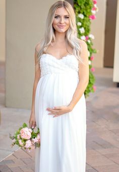 a pregnant woman in a white dress holding a bouquet