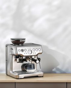 an espresso machine sitting on top of a wooden table next to a white wall