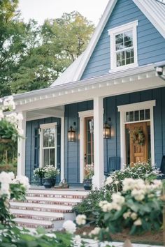 a blue house with white trim and flowers on the front door, steps leading up to it