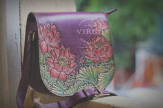 a purple purse with flowers painted on the front and side, sitting on a ledge