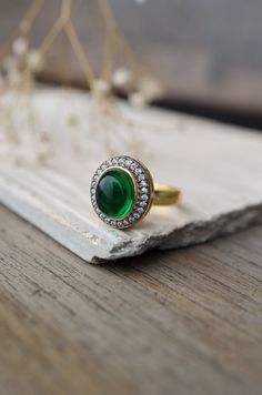 This elegant ring features a central green stone surrounded by sparkling cubic zirconia, adding a touch of glamour to any ensemble. Its versatility makes it perfect for complementing a variety of outfits and styles. Finish: 22KT Gold Plating Material: Silver, Copper Alloy, Polki Color: Green Size: One Size Closure Type: Adjustable Box Contains: 1 Ring Green Diamond Rings With Pave Setting, Green Emerald Ring With Pave Setting As Gift, Green Rings With Pave Setting For Formal Occasions, Green Diamond Ring With Gemstone Accents For Formal Occasions, Green Pave Setting Rings For Formal Occasions, Formal Green Rings With Pave Setting, Formal Green Diamond Ring With Gemstone Accents, Fine Jewelry Green Ring With Pave Setting, Green Rings With Pave Setting In Fine Jewelry Style