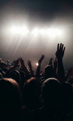 a crowd of people at a concert with their hands in the air and lights shining down on them