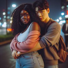 two people standing next to each other in front of a street at night with city lights behind them