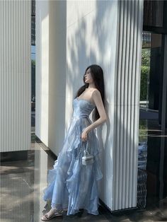 a woman in a blue dress leaning against a column